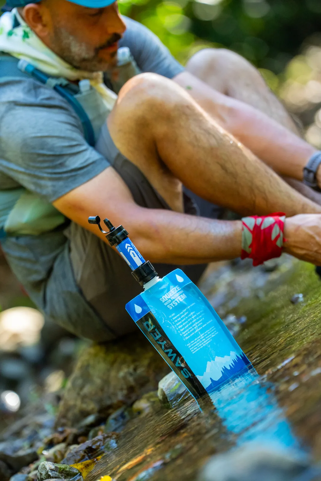 Runner filling a Sawyer filter bag in a jungle stream